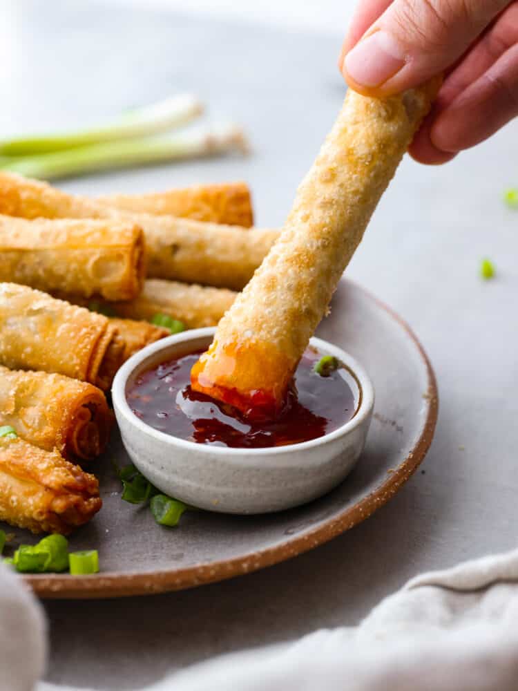 Close view of lumpia on a gray plate with a side of dipping sauce. Sliced onions garnished on top.