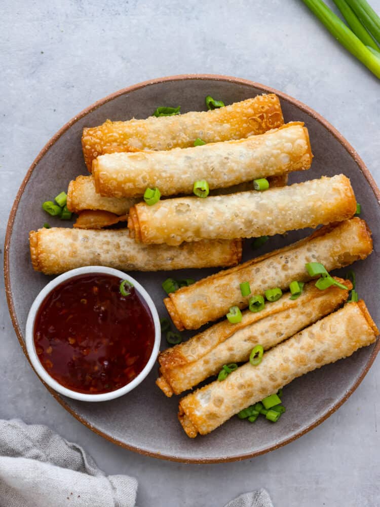 Top view of lumpia on a gray plate with a side of dipping sauce. Chopped green onion on top for garnish.