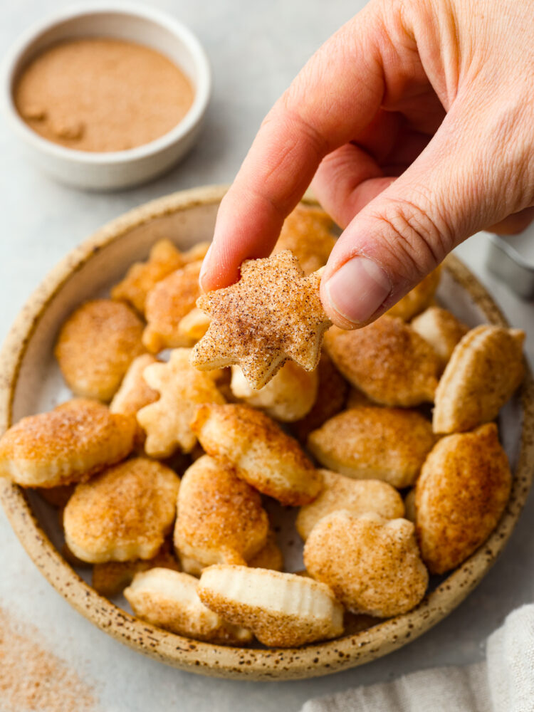 Close view of pie crust cookies on a small stone plate. A cookie is being lifted off the plate.