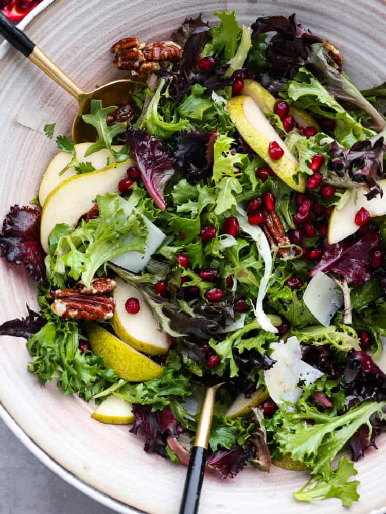 A close up top view of a pomegranate salad with gold tongs. 