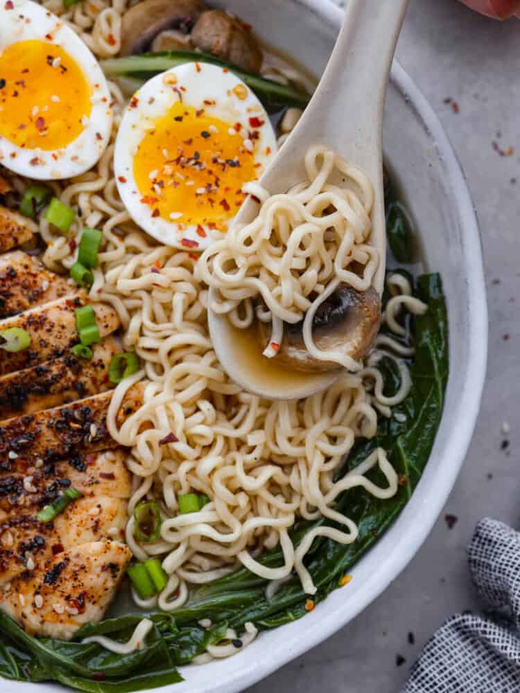 Closeup of ramen with noodles, a sliced mushroom, and broth in a white spoon.