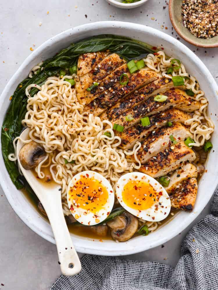 A bowl of chicken ramen with eggs and a white spoon.