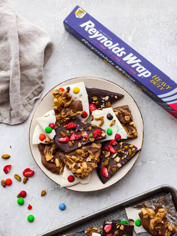 A plate of white chocolate bark, dark chocolate bark and milk chocolate bark with a Reynolds Wrap Foil package next to it. 