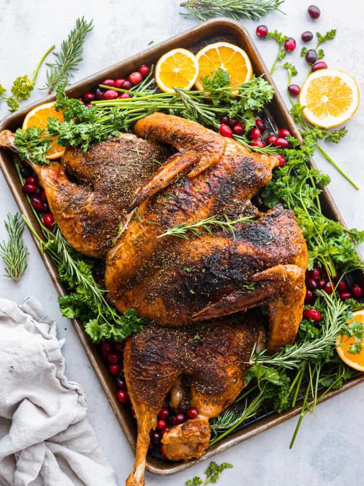 A spatchcock turkey roasted on a pan with oranges, cranberries, and fresh herbs.