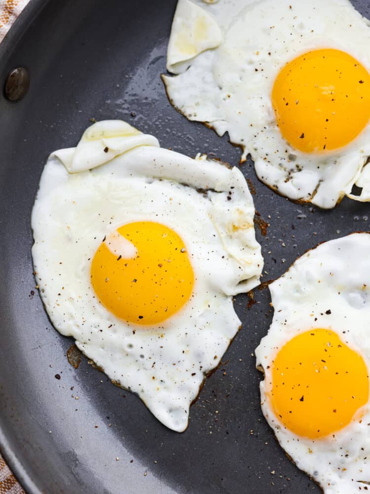 A close up of sunny side up eggs cooked in a frying pan.