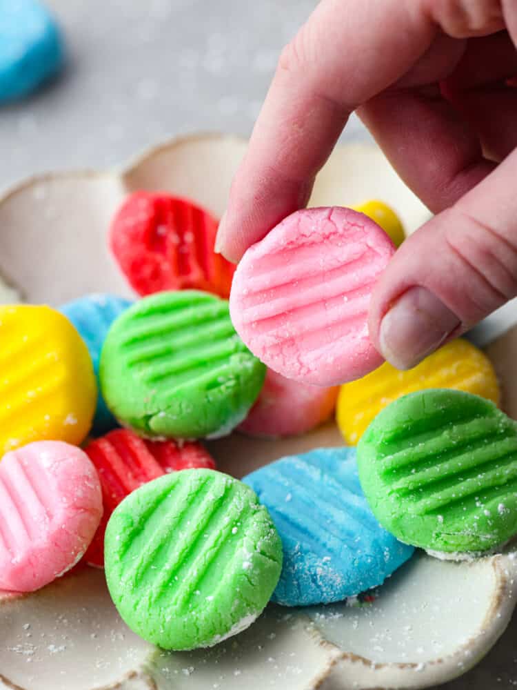 A hand holding a pink cream cheese mint above a platter of other mints.