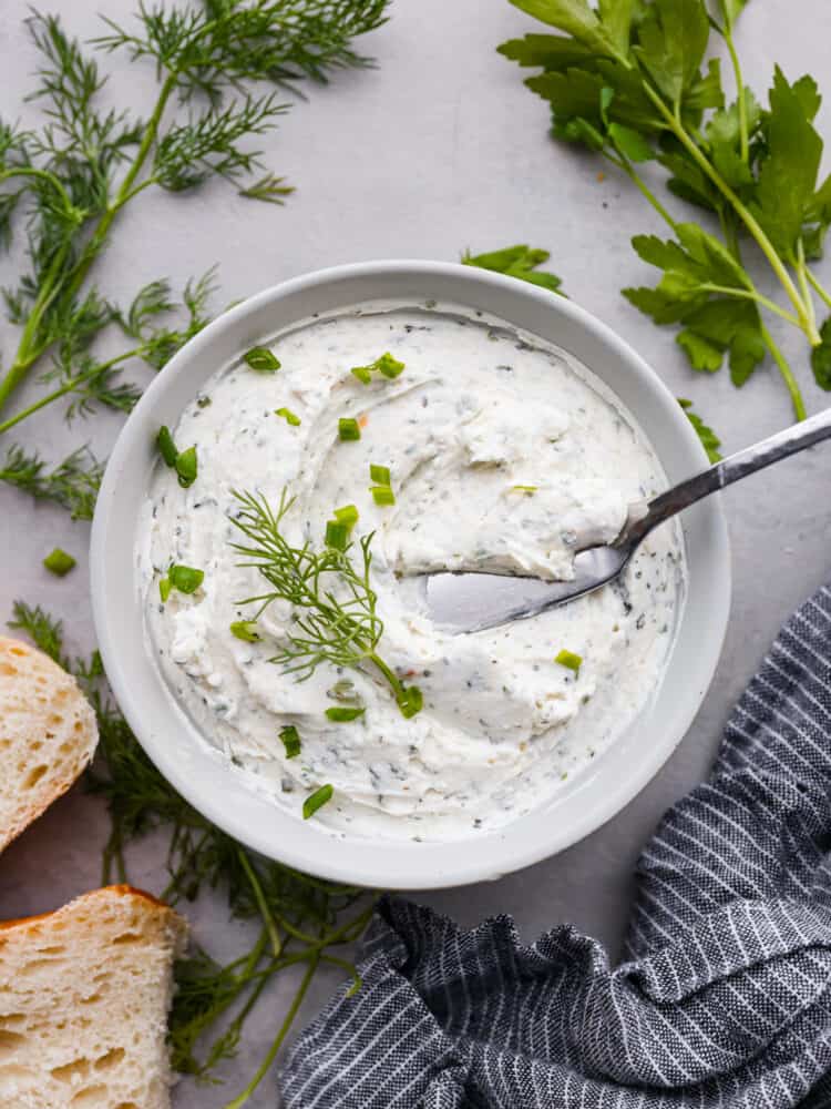 Garlic herb cream cheese spread in a bowl with fresh herbs around it.