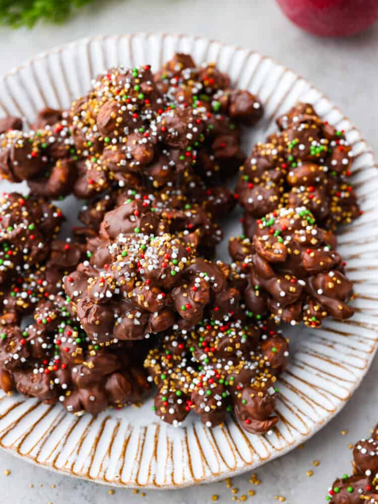 The crockpot candy on a white plate with sprinkles around the plate.