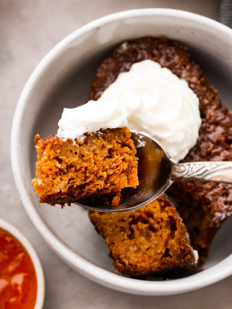 A bite of pudding and whipped cream in a silver spoon.