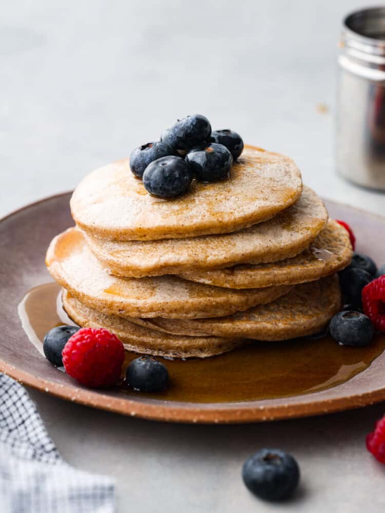 Close view of protein pancakes on a brown plate garnished with fresh blueberries, raspberries, and maple syrup.