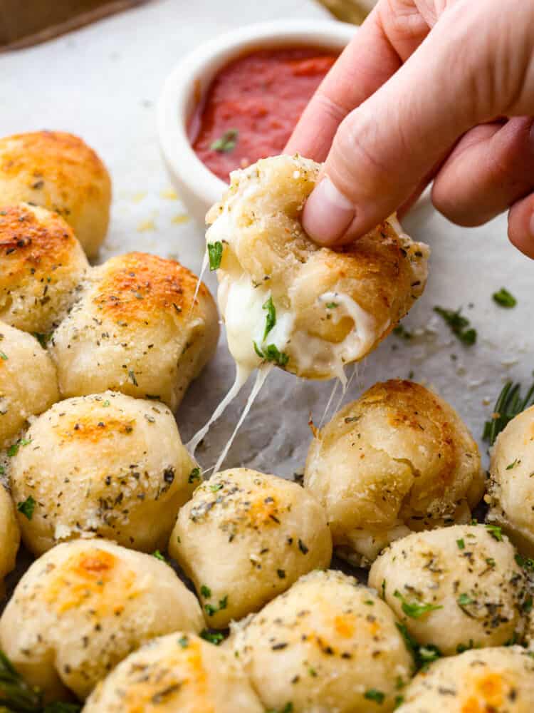 A close up of Christmas tree pull apart bread with a hand pulling up one of the rolls.