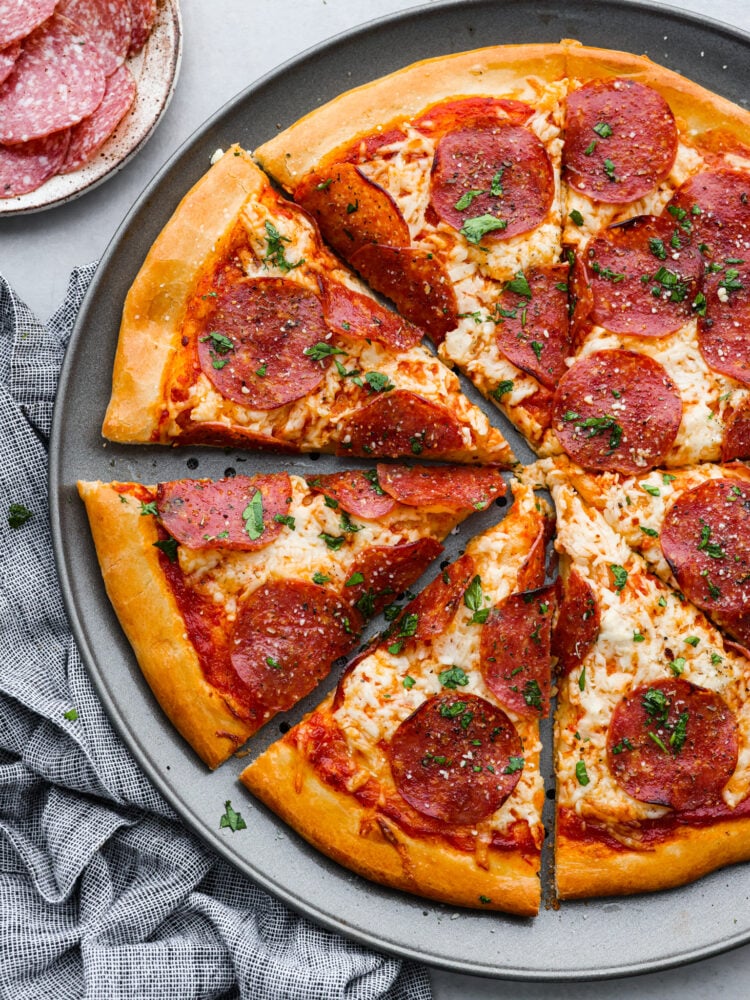 Salami pizza on a pizza pan cut into slices.