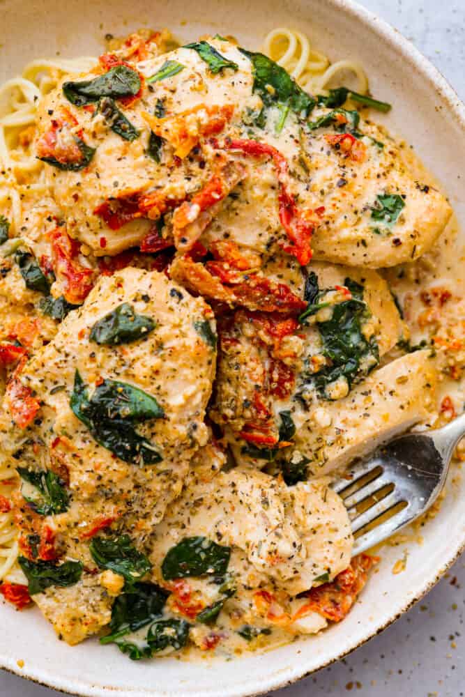 Creamy crockpot Tuscan chicken on a plate with noodles.