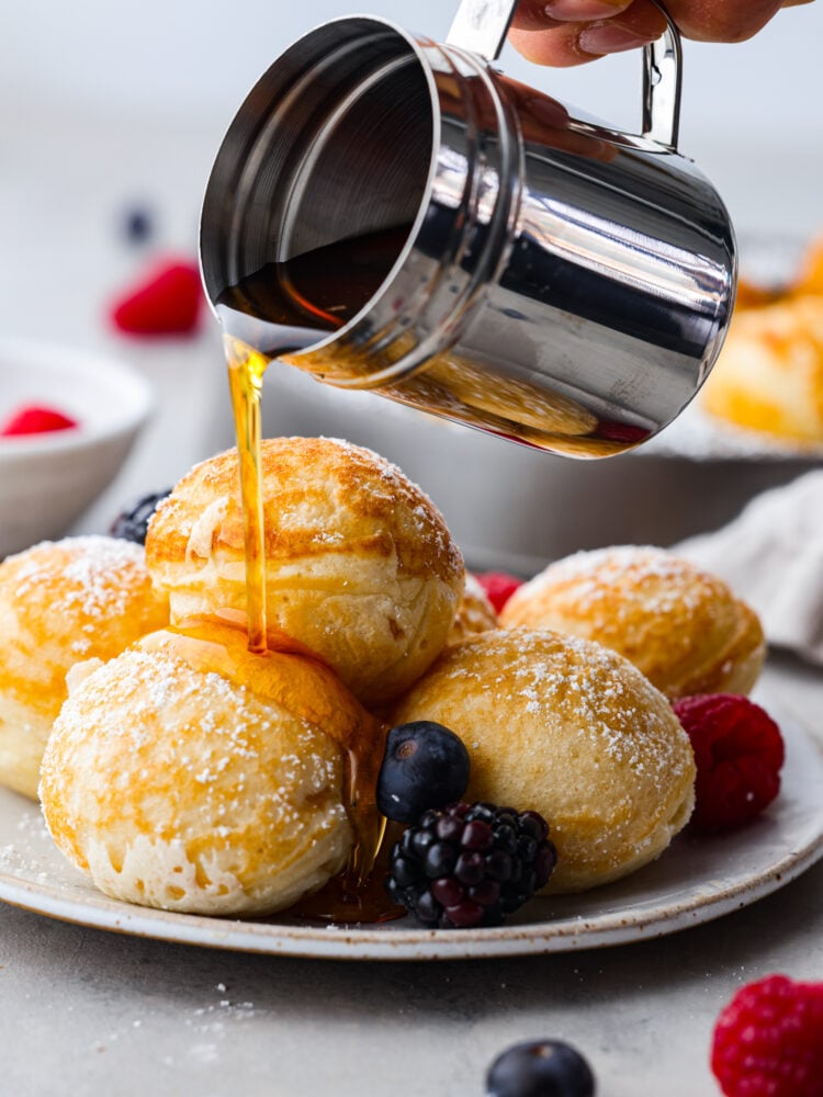 Ebelskivers on a plate with syrup being poured over them.