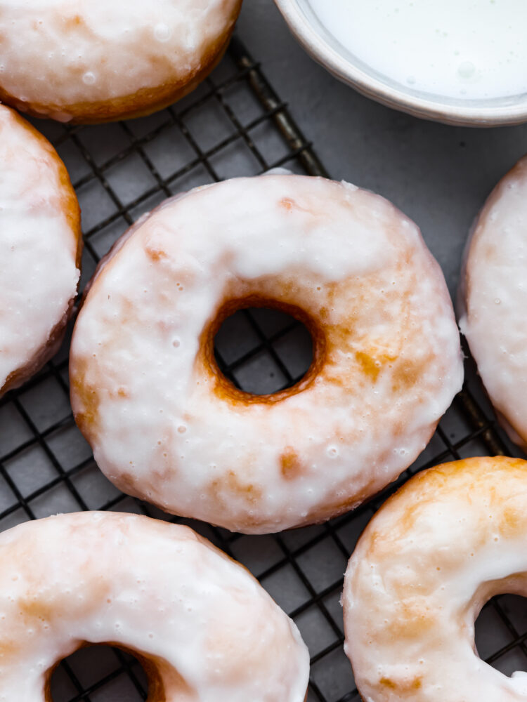 A close up on glazed donuts on a drying rack.