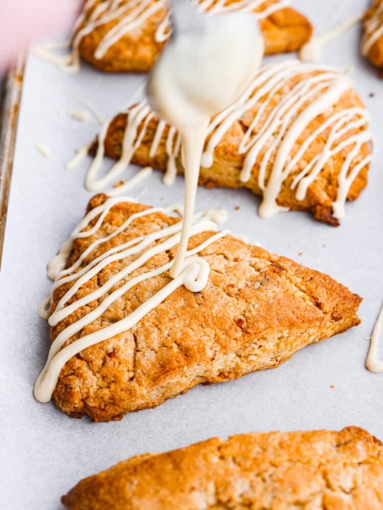 A spoon drizzling maple glaze over the top of the scone.