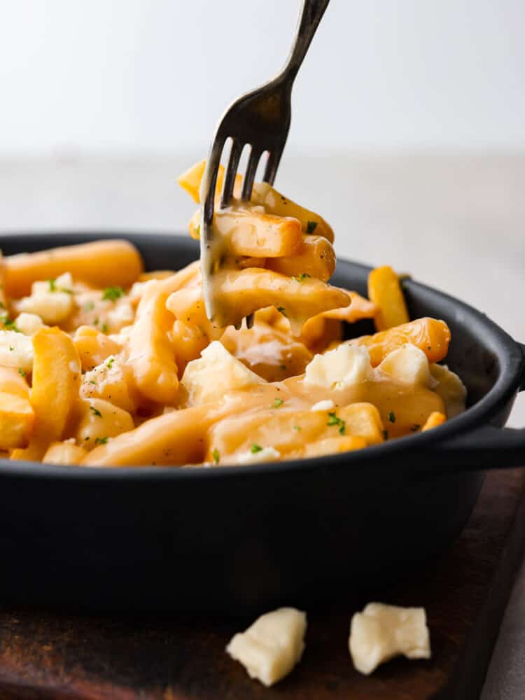 Poutine in a dish with a fork taking a piece of it.