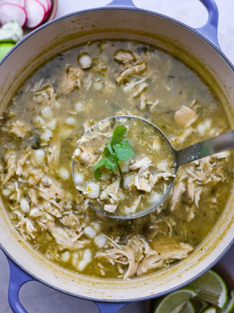 The pozole in a pot with a ladle taking a spoonful out.