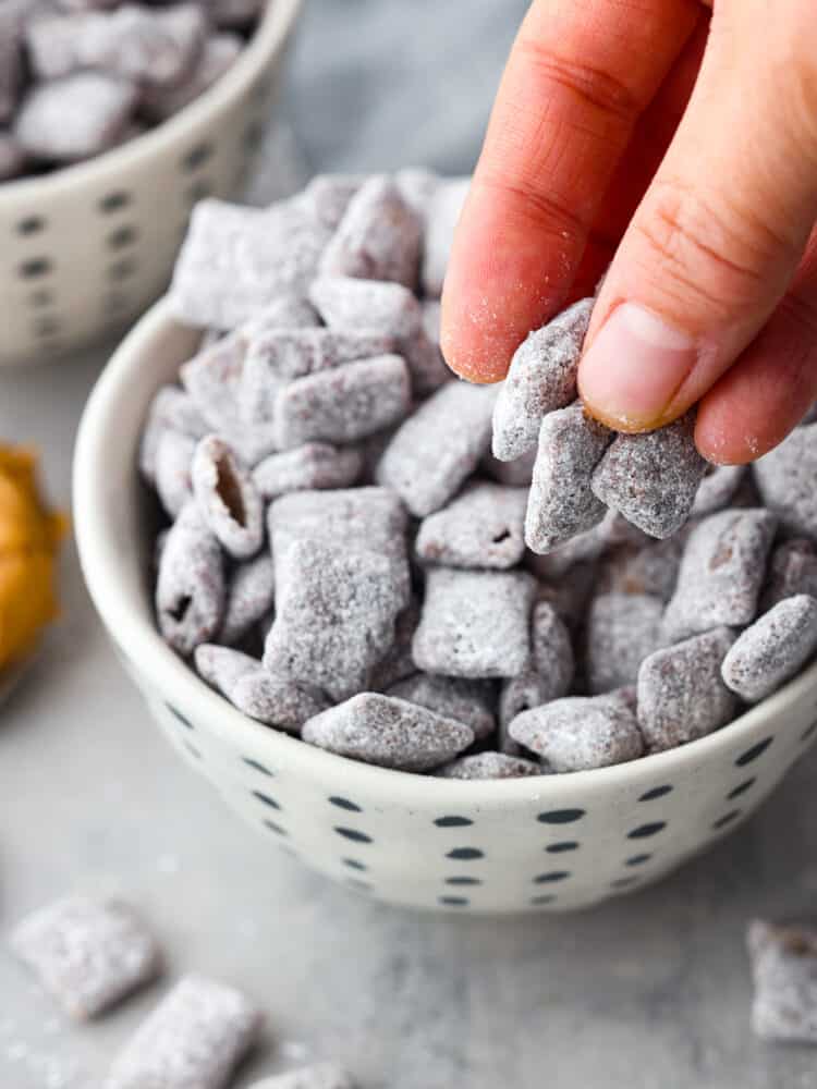 A hand grabbing the chex mix snack out of the white and black bowl