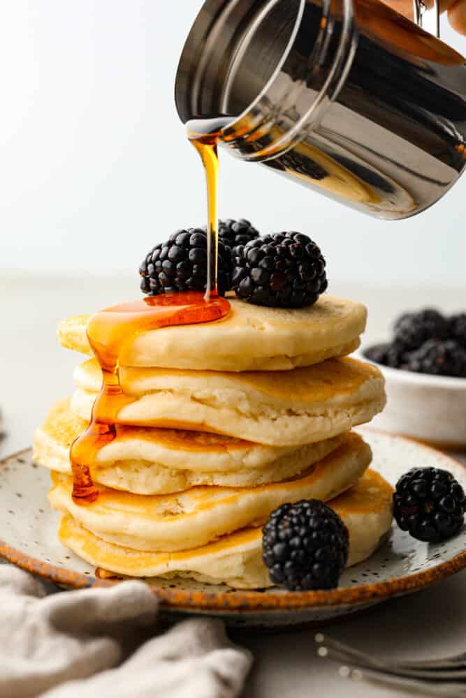 Pouring maple syrup over a stack of pancakes.