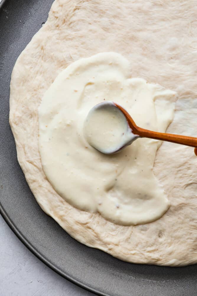 A spoon spreading the sauce over pizza dough.