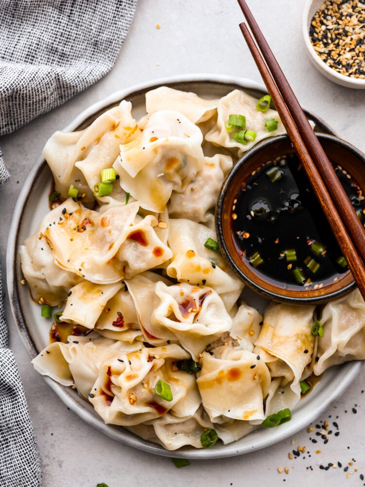 Top-down view of boiled wontons served on a white plate with soy sauce.