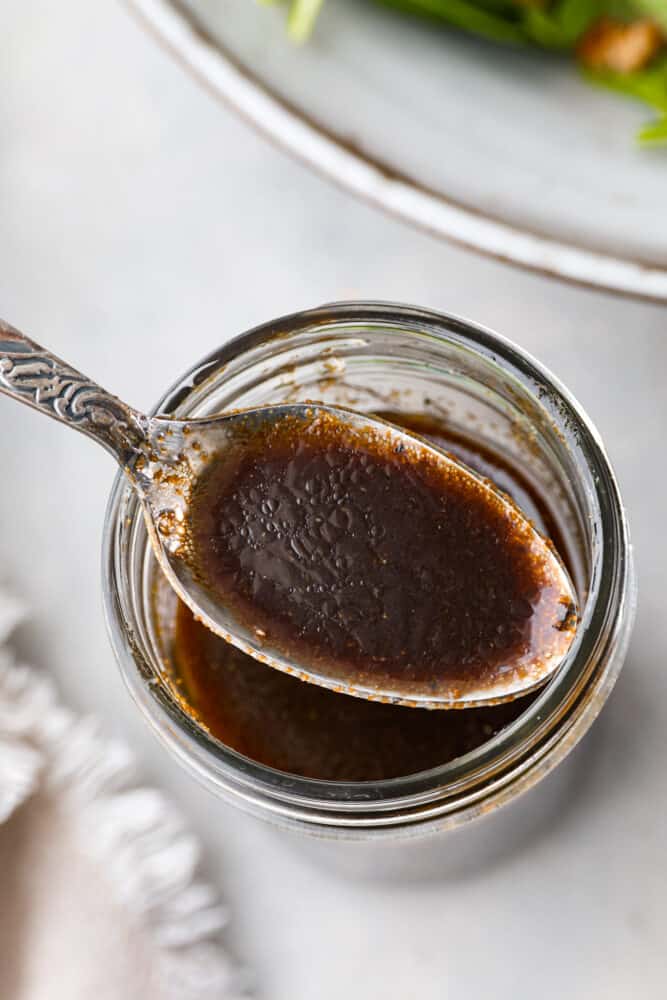 A close up on the balsamic vinaigrette on a spoon over a mason jar.