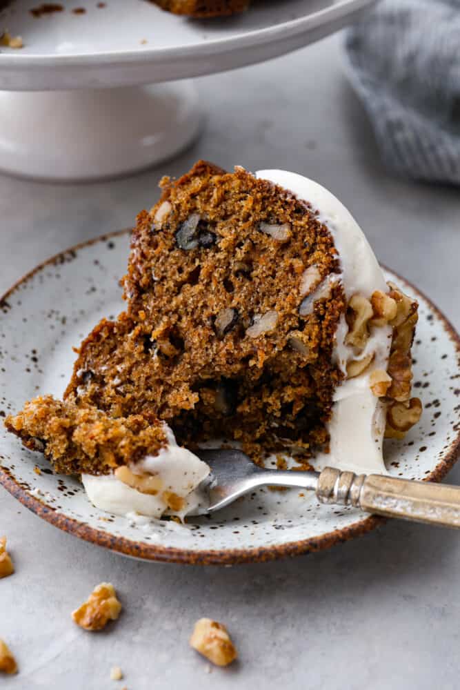 A piece of carrot bundt cake on a plate with a fork taking a scoop out.