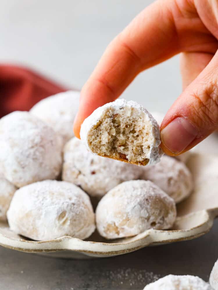 A hand holding a Mexican wedding cookie with a bite taken out of it.