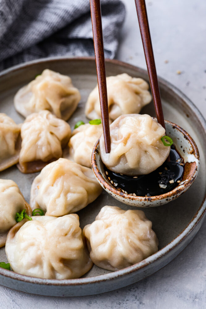 Soup dumplings being dipped in sauce with chop sticks.