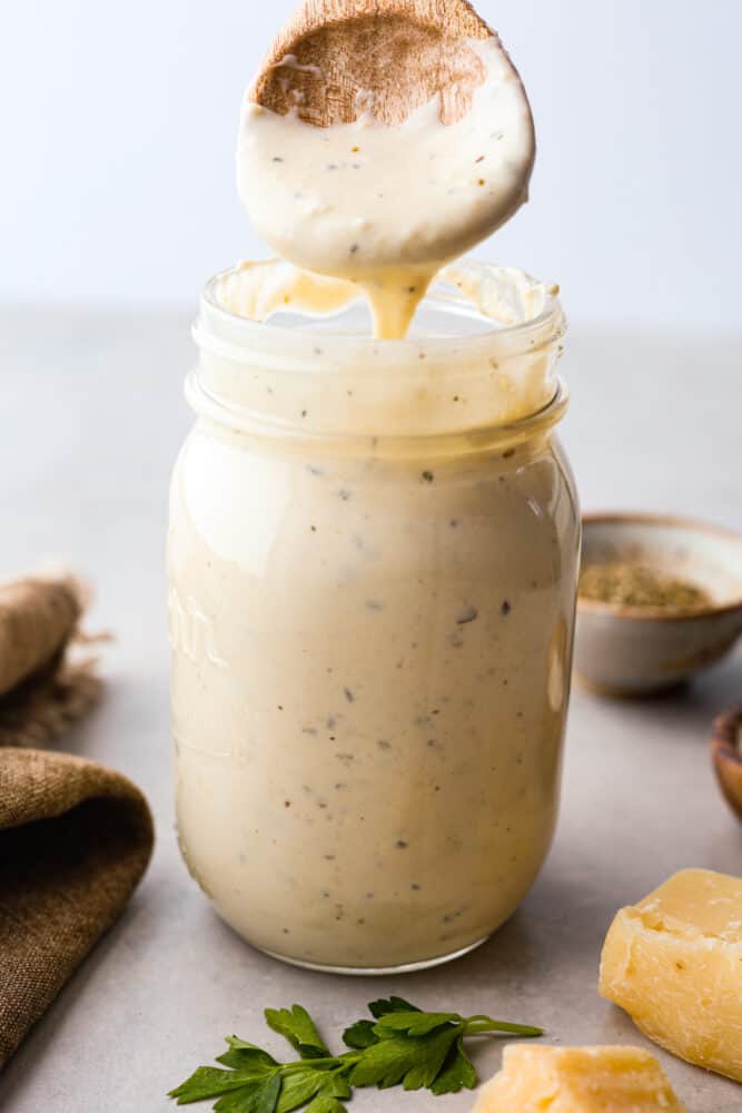 Pouring alfredo sauce into a glass jar.