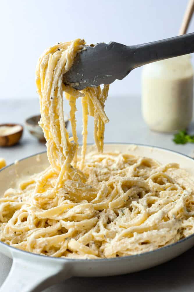 Using tongs to pick up fettuccine alfredo.