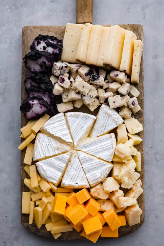 Top-down view of an assortment of cheeses on a wooden board.