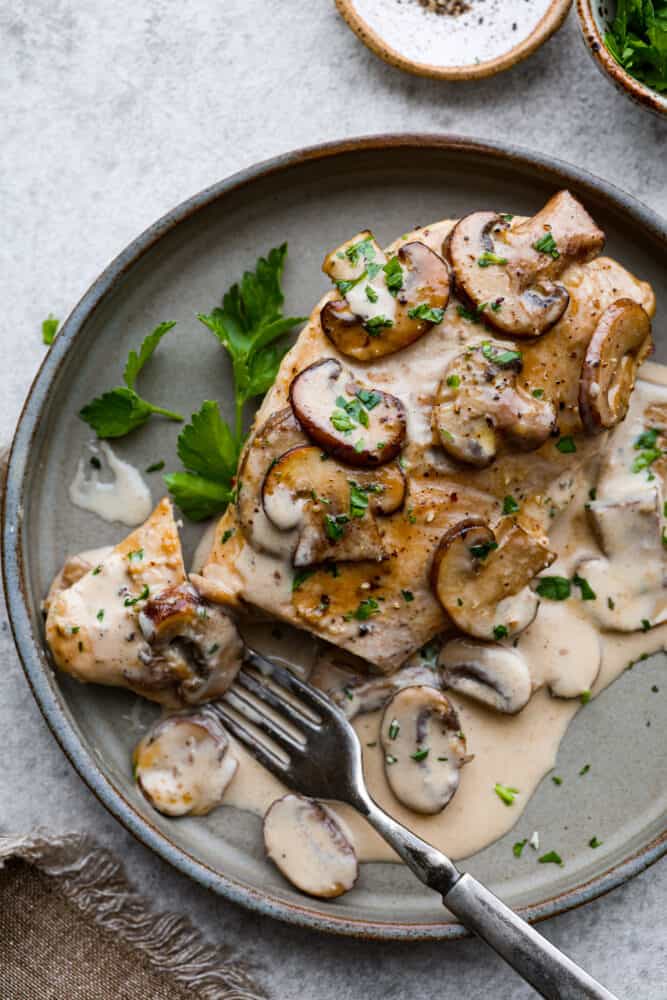 A piece of chicken on a plate with a fork taking a bite out of it.