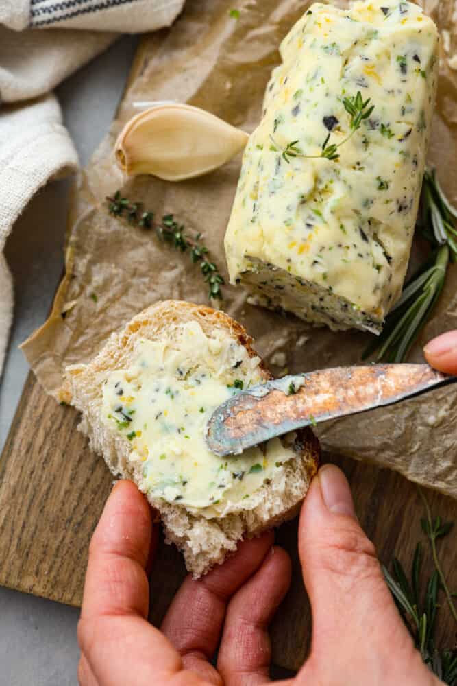 An overhead view of compound butter with someone spreading some on a piece of bread.