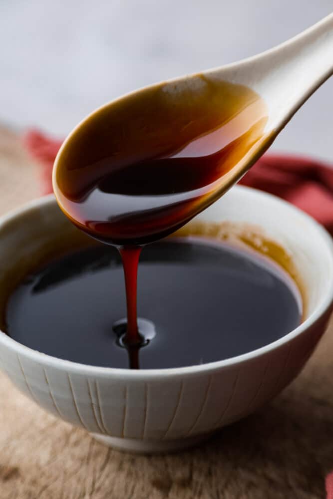 Eel sauce being poured out of a spoon into a bowl.