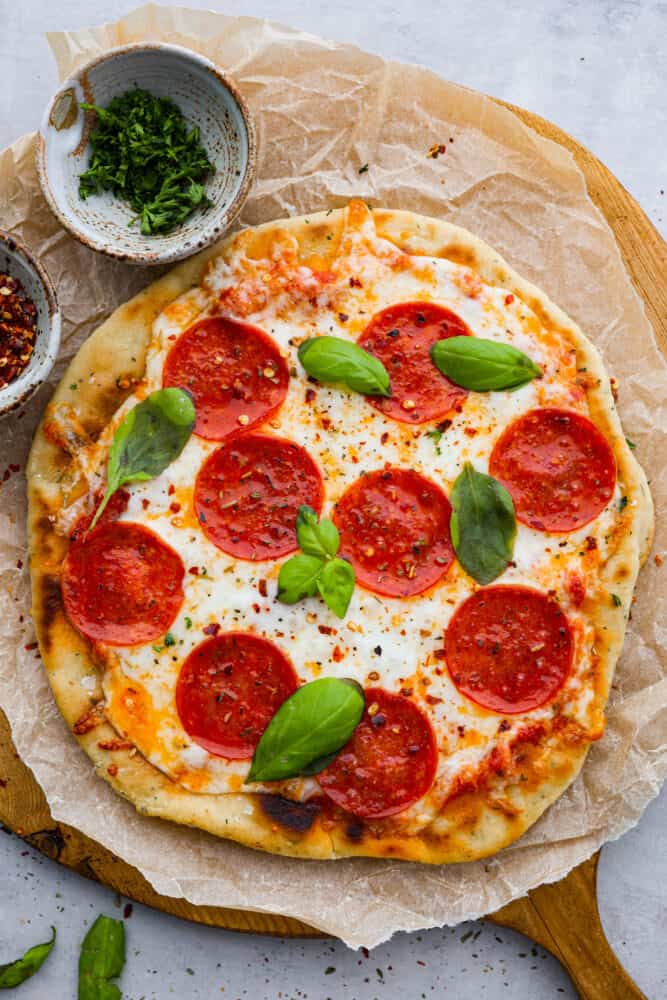 Flatbread pizza on a piece of parchment with fresh basil on top.