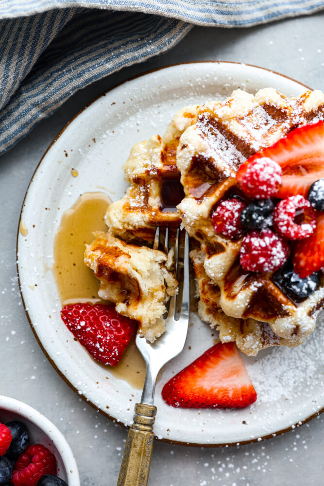 A liege waffle on a plate with a bite being scooped out with a fork.