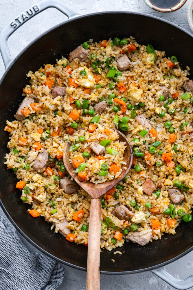 A pot of pork fried rice with a wooden spoon in it.