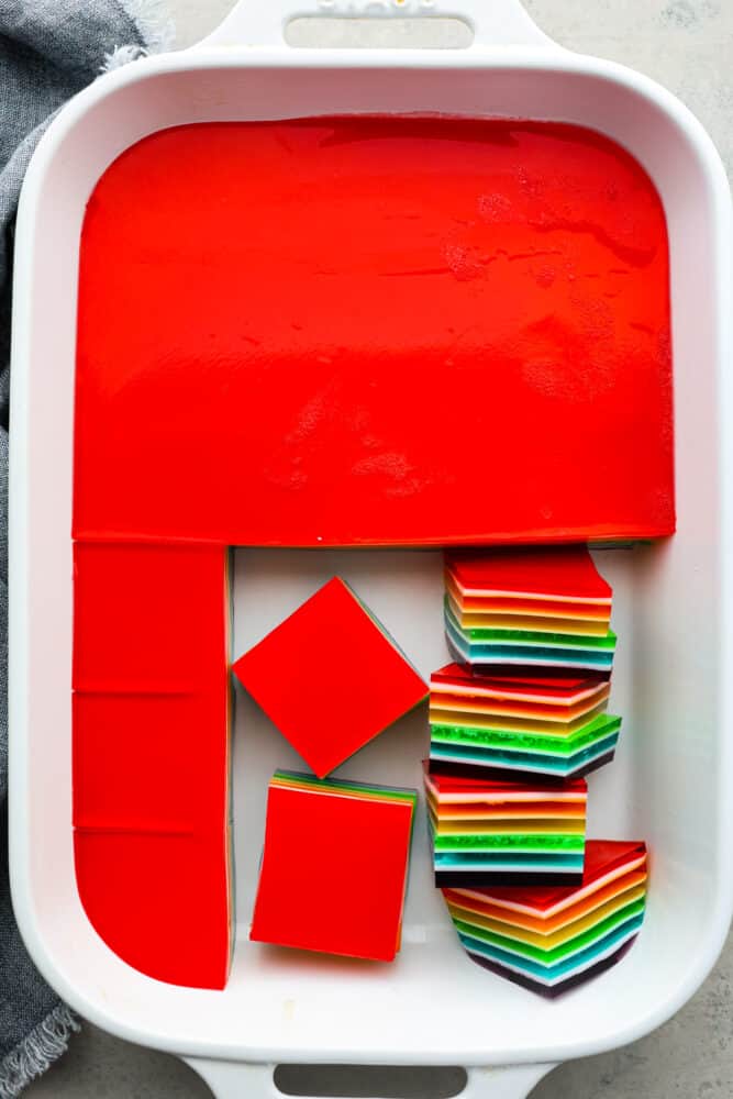 Top-down view of a pan of rainbow jello being cut into squares.