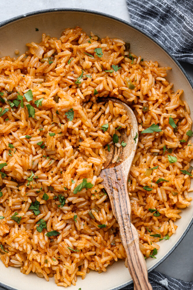 A close up of the Spanish rice in the skillet with a wooden spoon.