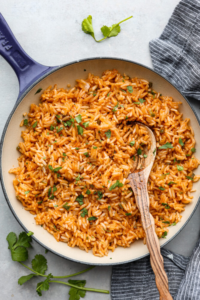 Spanish rice in a skillet with a wooden spoon in it.