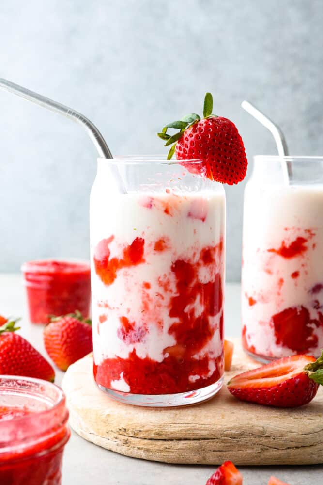 2 glasses of strawberry milk served on a wooden board.