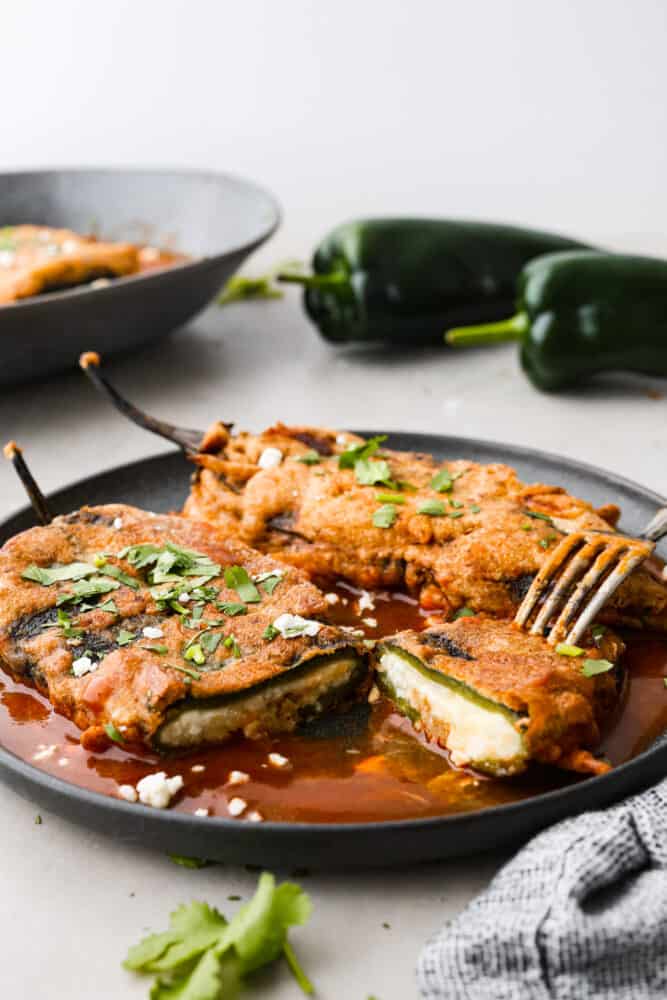 2 chile rellenos on a plate, with one cut in half.