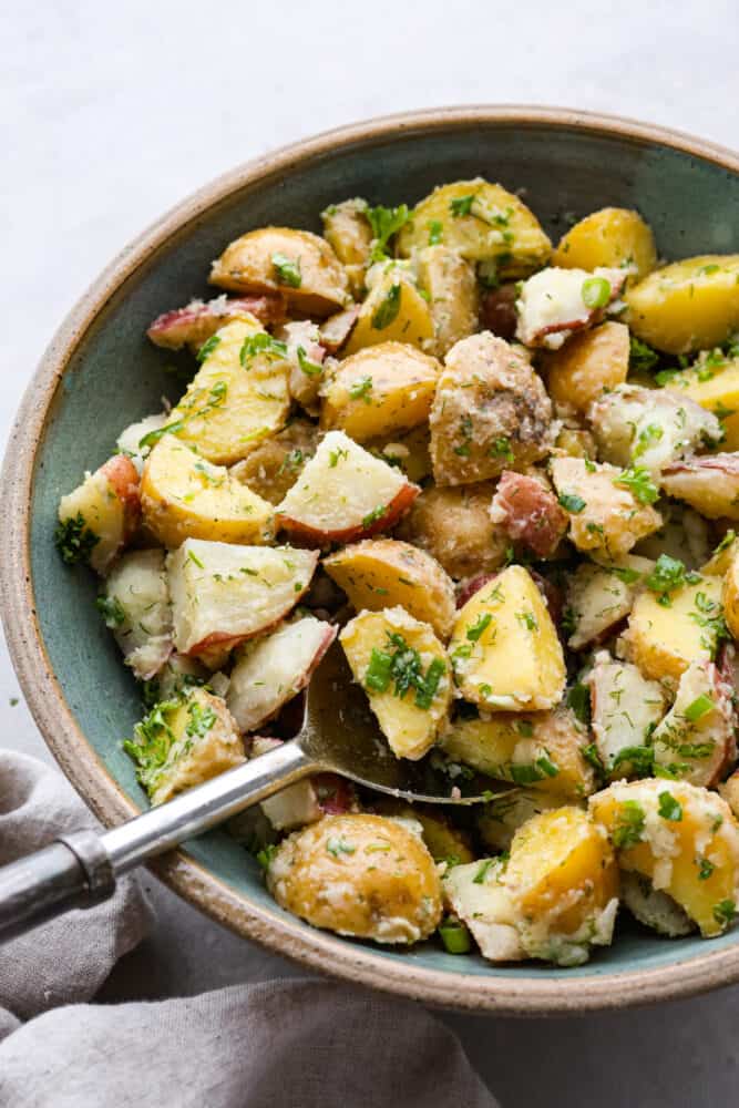 Potato salad being served with a large metal spoon.