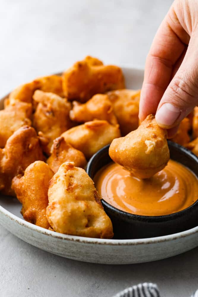 Dipping a piece of fried cauliflower into a creamy orange sauce.