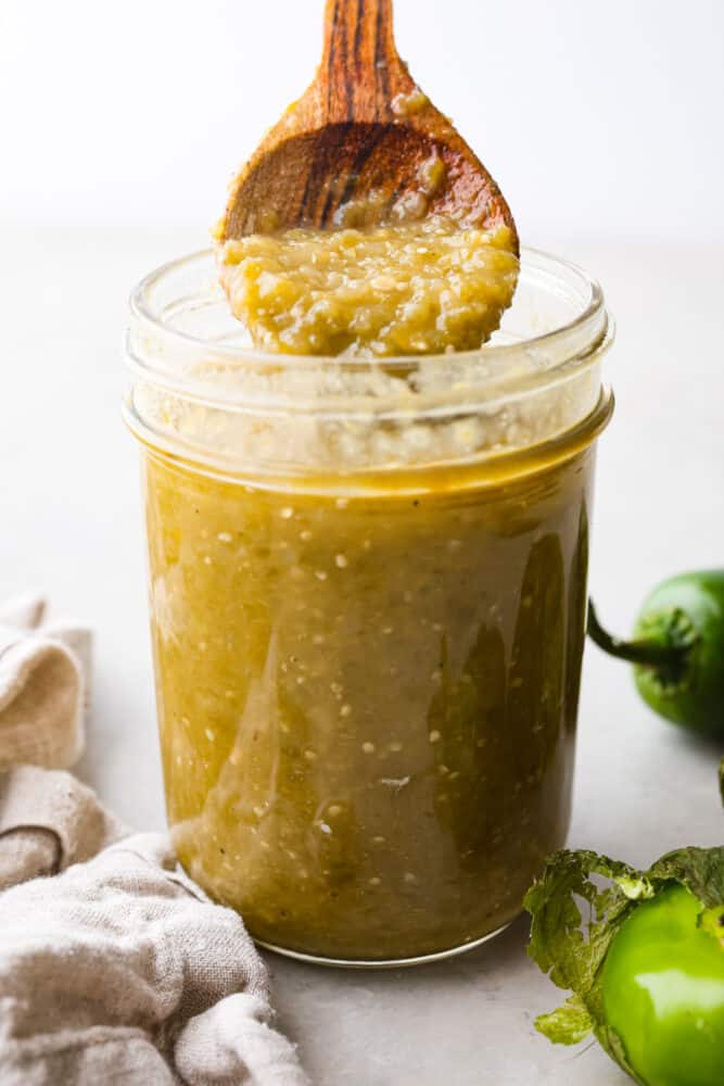 A jar of homemade green enchilada sauce with a wooded spoon scooping some out. 