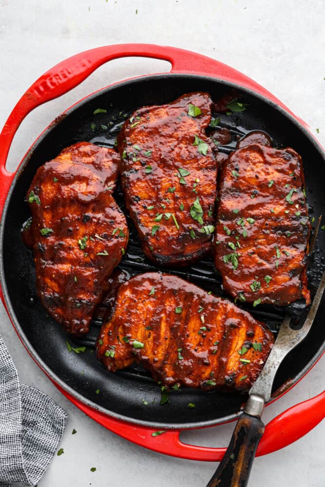 The top view of 4 cooked bbq pork chops in a a red pan. 