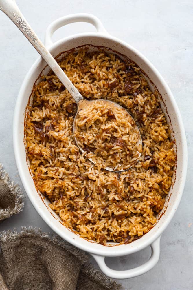 The top view of baked rice in a casserole dish with a large spoon. 