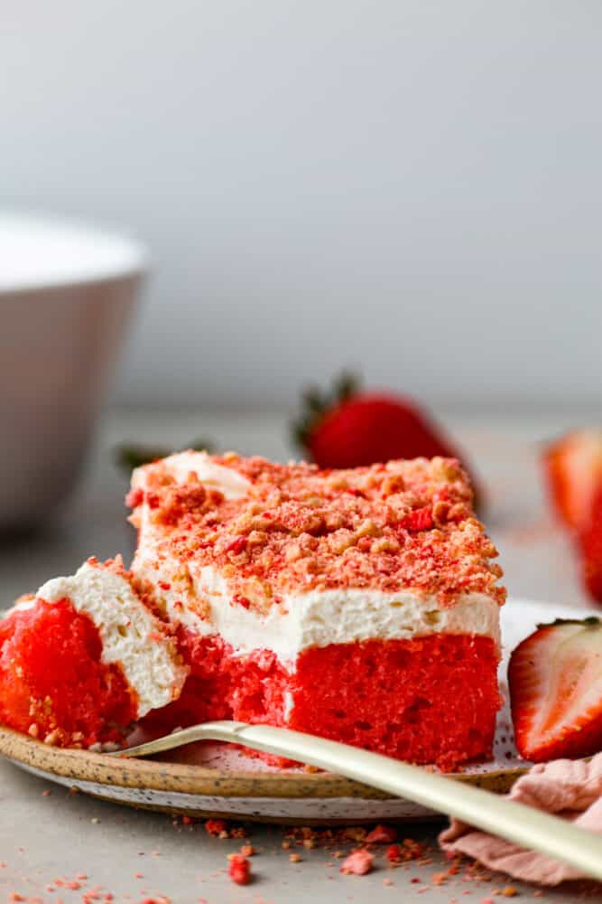 A piece of strawberry crunch cake on a plate with a gold fork. 